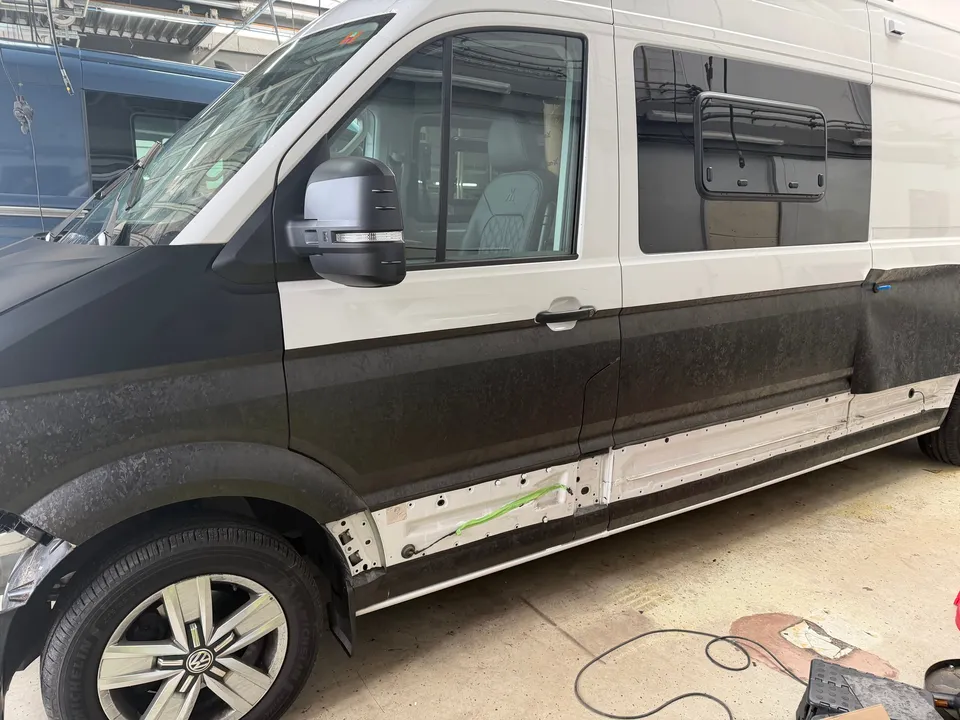 Camper tijdens het wrappen: zijkant met deels beplakte onderzijde