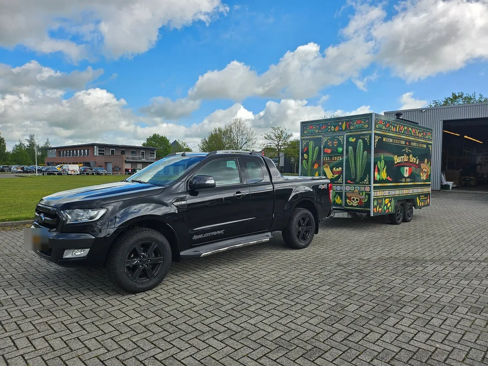 Foodtruckaanhanger achter een zwarte pick-up op een parkeerplaats