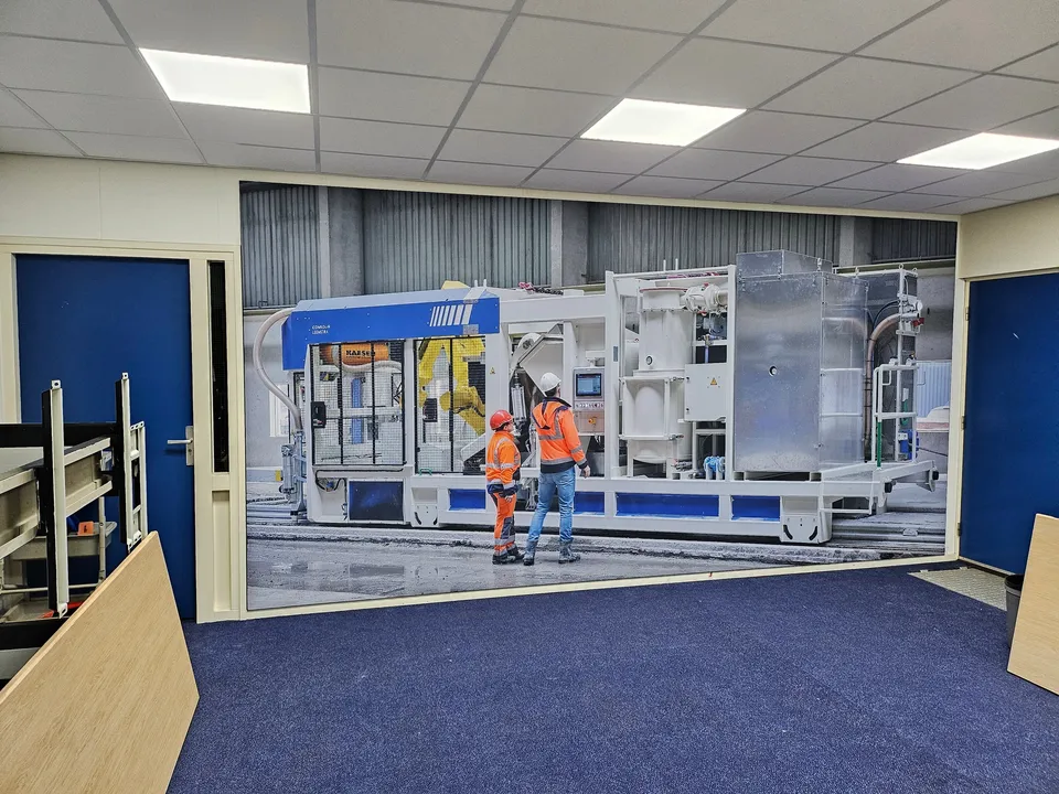 Wandprint met bouwmachine en twee werknemers in een kantoorruimte
